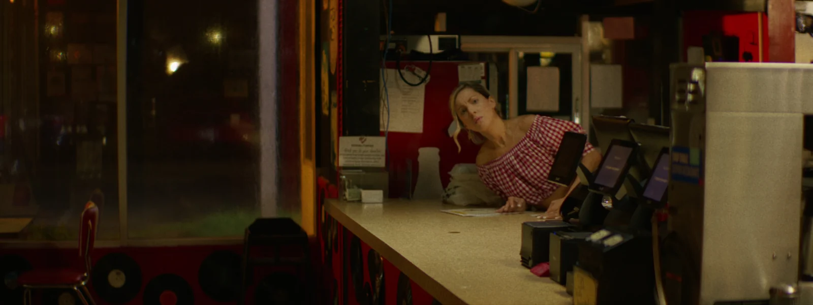 A waitress leans across the counter of an empty diner late at night