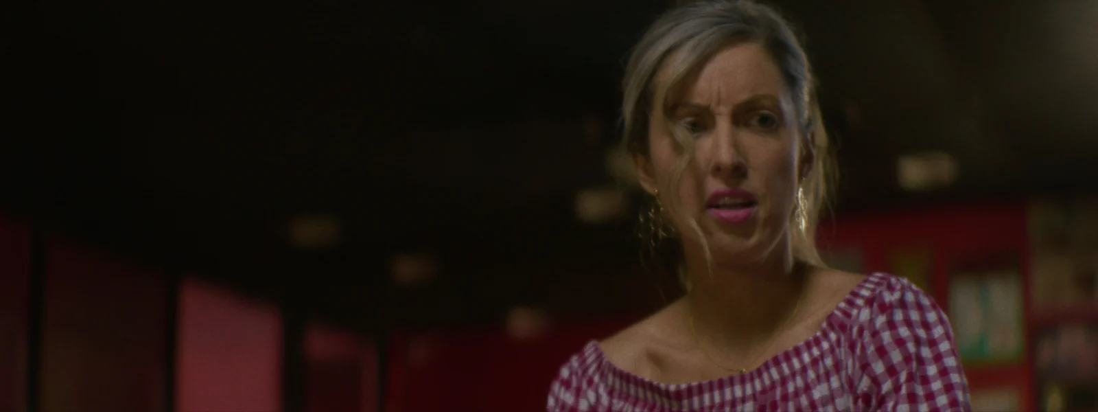 A waitress in a red gingham top reacts to something across the diner